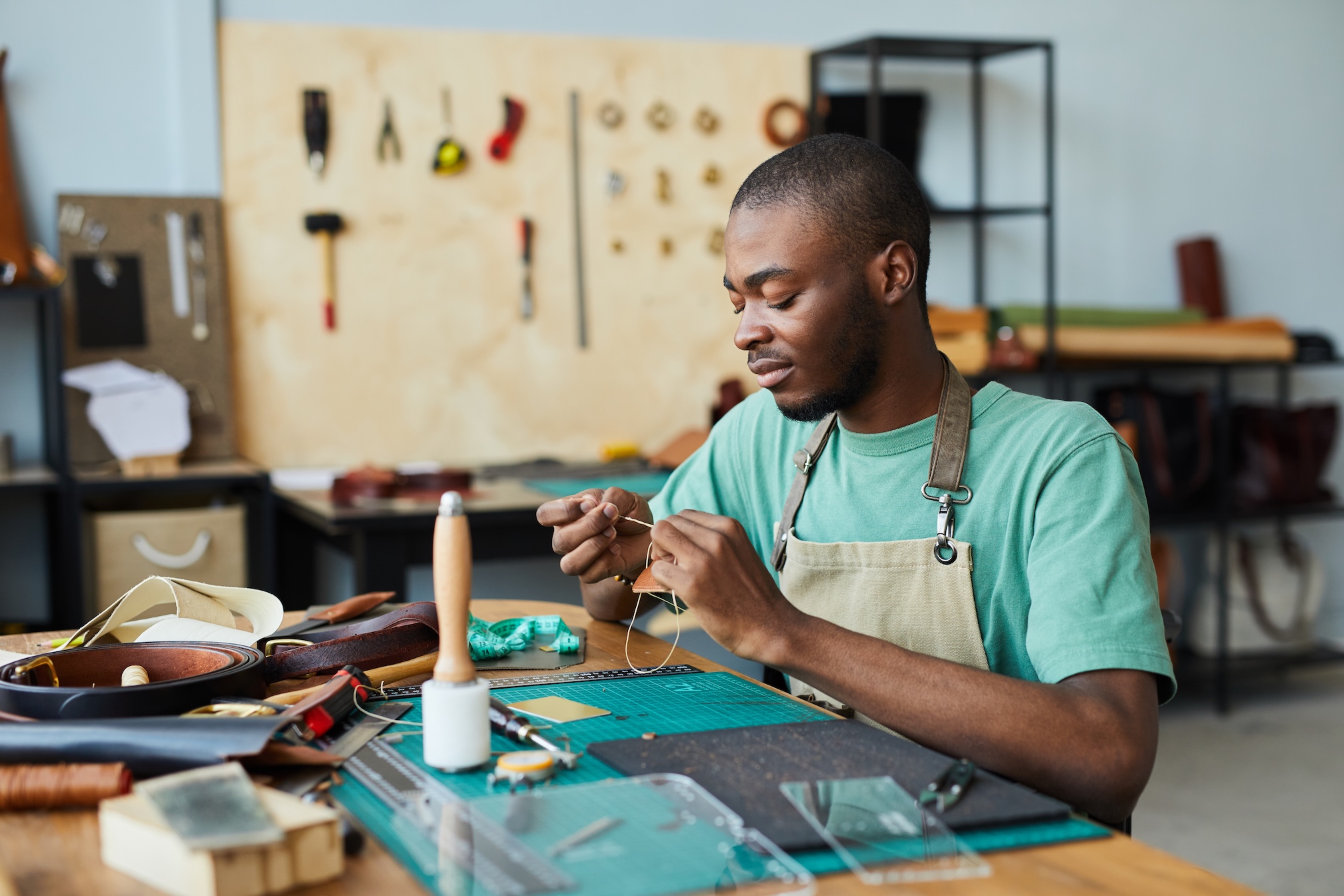 A leatherworker stitching a piece by hand at his workbench